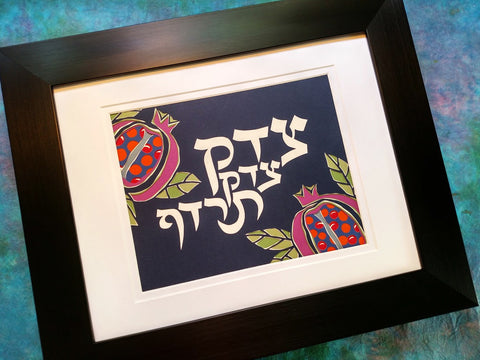 An unframed papercut artwork with a Jewish theme, featuring the text 'Tzedek tzedek tirdof' on a dark background with colorful illustrations of fruits and flowers.